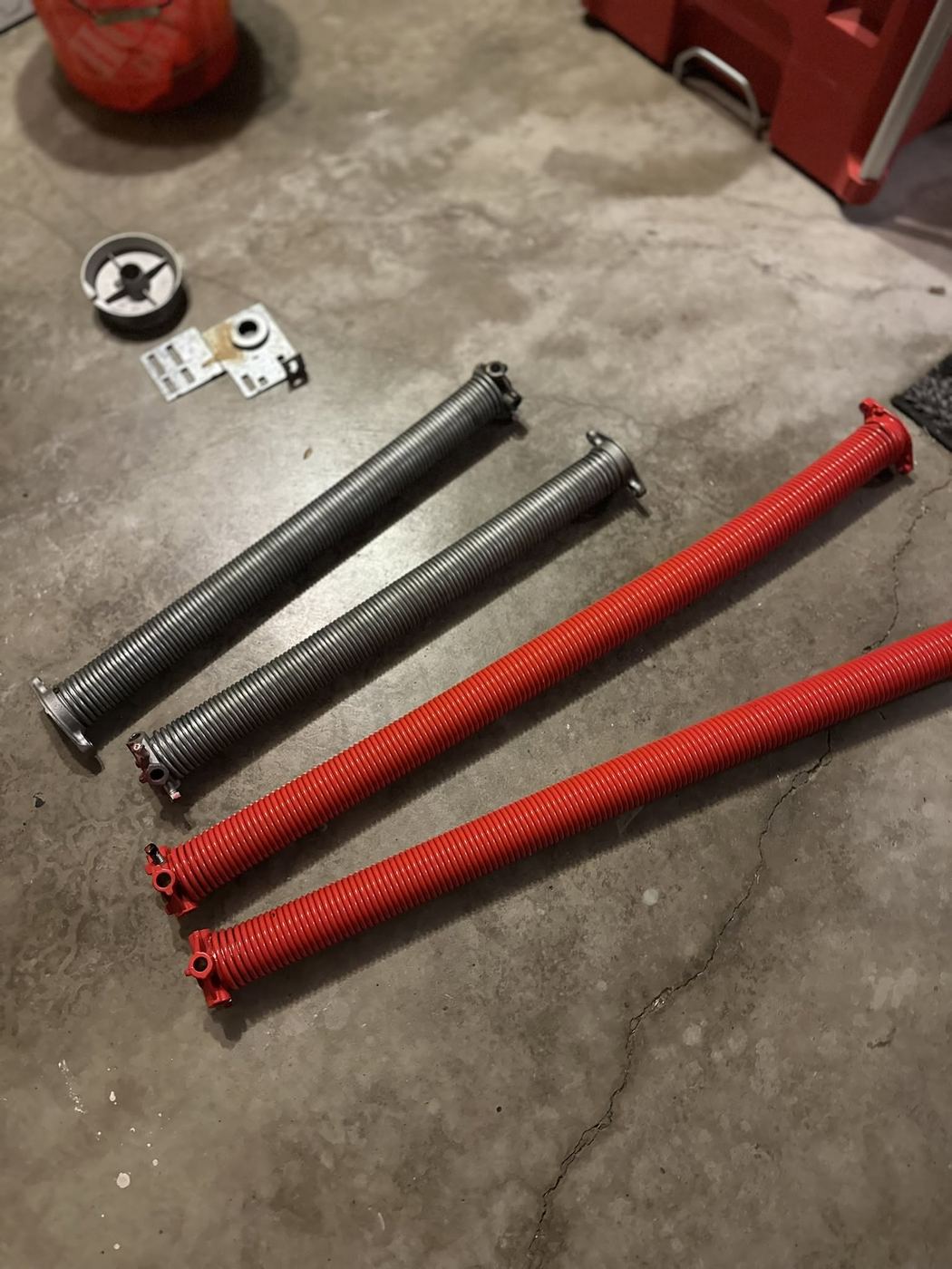 Old broken garage door torsion springs next to new replacement springs